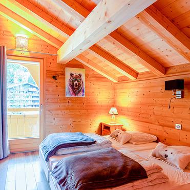 Holzverkleidetes Schlafzimmer mit zwei Betten, Fenster mit Vorhang und einem Tierbild an der Wand. Gemütliche Atmosphäre.