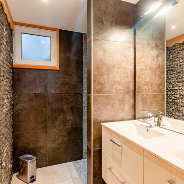 Modernes Badezimmer mit Dusche, Waschbecken, dekorativen Steinwänden und Fenstern. Holz- und Steinmaterialien kombiniert.