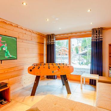 Wohnzimmer mit holzverkleideten Wänden, einem Tischfußballtisch, Fernseher und Blick auf schneebedeckte Landschaft.