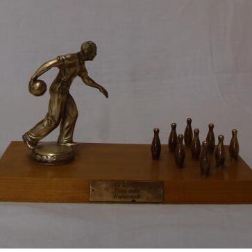 Statuette eines Bowlingspielers, der einen Ball auf eine Reihe von neun Kegeln wirft, auf einem Holzsockel.