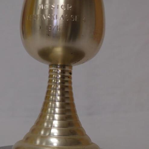 Silberner Pokal auf einem runden Sockel, mit eingeprägtem Text "Meister Medenklasse 4 1976".