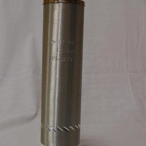 Trophäe aus Metall mit goldenem Aufsatz und gravierter Inschrift „Erster Platz“.