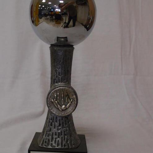 Pokalschale mit reflektierender Oberfläche und gravierter Siegerplakette, auf grauem Sockel mit Beschriftung.