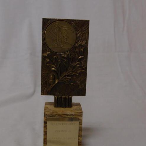 Bronzene Auszeichnung mit gravierter Medaille und floralem Muster auf einem marmorierten Sockel.