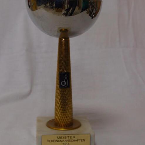 Silberner Pokal mit goldenem Fuß, beschriftet mit „MEISTER VEREINSMANSCHAFTEN 1984 SKC-Gresheim“ auf marmorner Basis.
