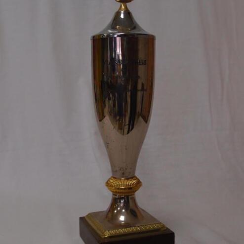 Silberner Pokal mit goldener Verzierungen auf einem dunklen Sockel, präsentiert auf einem neutralen Hintergrund.