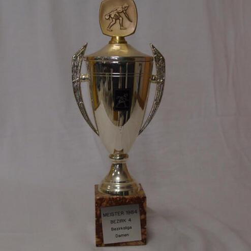 Pokal mit goldenem Deckel und gravierter Figur, beschriftet mit „Meister 1984 Bezirk 4 Damen“.