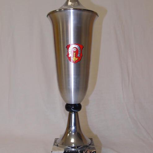 Trophäe aus Metall mit schmuckvollem Griff und Wappen auf schwarzem Marmorsockel, Hintergrund einfarbig.