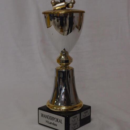Wanderpokal mit goldenen und silbernen Elementen, beschriftet mit „H. Landau“ und Jahreszahlen auf schwarzem Sockel.