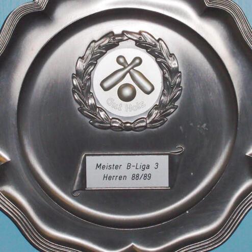 Silbernes Meisterschaftsschild mit Wappen und Beschriftung „Meister B-Liga 3 Herren 88/89“ an blauer Wand.