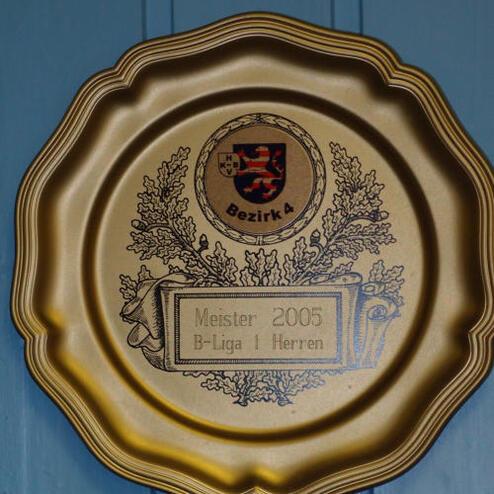 Goldene Meisterschaftsplakette von 2005 für B-Liga Herren, verziert mit einem Wappen und Pflanzenmotiven.
