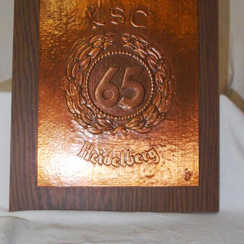 Kupferne Plakette zum 65-jährigen Jubiläum des KSC, montiert auf einem Holzrahmen mit der Inschrift „Heidelberg“.