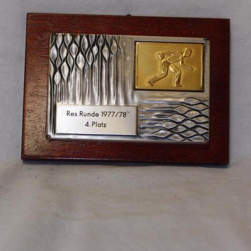 Holzplatte mit einer Metallauszeichnung, graviert mit "Res. Runde 1977/78" und "4. Platz", zeigt einen sportlichen Bewegungsablauf.