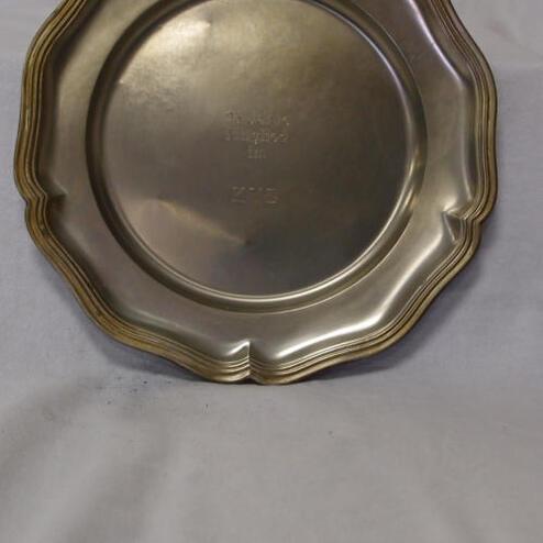 Silberner Teller mit geschwungenem Rand und Prägung in der Mitte, vor einem weißen Hintergrund.