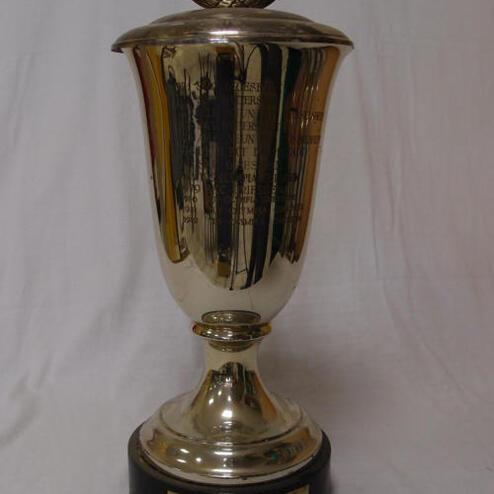 Silberner Wanderpokal mit Deckel und gravierten Schriftzügen auf schwarzem Sockel.