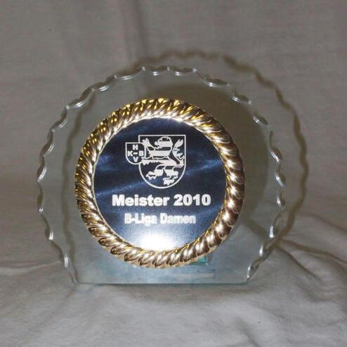 Glas-Trophäe mit goldener Umrandung, Beschriftung „Meister 2010 B-Liga Damen“ auf dunkelblauem Hintergrund.