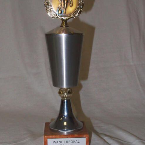 Wanderpokal aus Metall mit goldener Figur und gravierter Holzplatte, beschriftet mit „WANDERPOKAL H. Landau“.