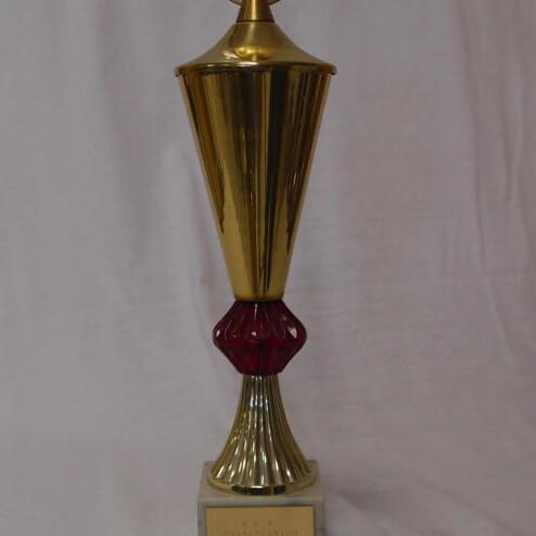 Goldener Pokal mit rotem Sockel und der Abbildung eines Athleten auf der Oberseite. Beschriftung an der Basis sichtbar.