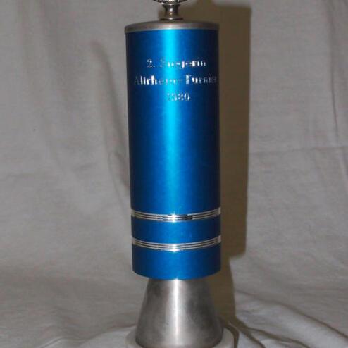 Silberner Pokal mit blauer Figur, gravierten Texten und runder Fußplatte aus Marmor.