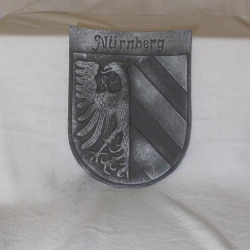 Metallisches Wappen von Nürnberg mit einem Adler und diagonal gestreiftem Feld in Schwarz und Silber.