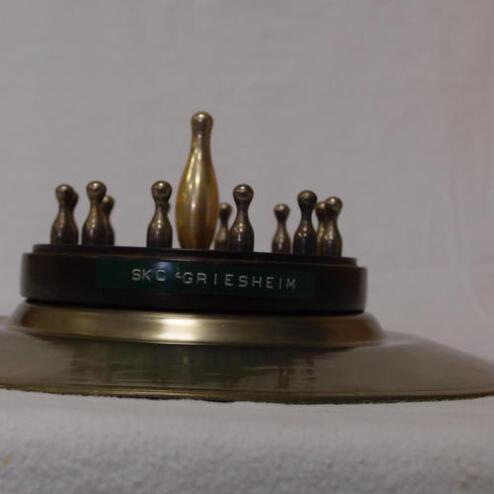 Pokalteller mit einer goldenen Musikantenfigur und mehreren Metallfiguren auf einem weißen Hintergrund.