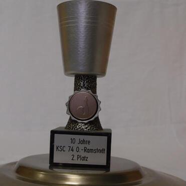 Silberner Pokal mit schwarzem Sockel, beschriftet mit „10 Jahre KSC 74 O.-Ramstadt 2. Platz“.
