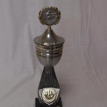 Silberner Pokal auf schwarzem Sockel mit Inschrift „2. Platz KVD-VMM“ und Kranz-Emblem oben.