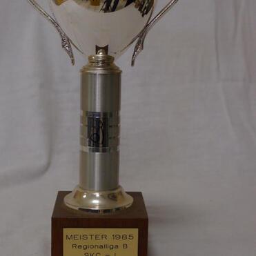 Silberner Pokal auf Holzsockel mit der Inschrift „MEISTER 1985, Regionalliga B, SKC - I“.
