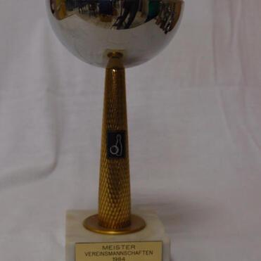 Silberner Pokal mit goldenem Fuß, beschriftet mit „MEISTER VEREINSMANSCHAFTEN 1984 SKC-Gresheim“ auf marmorner Basis.