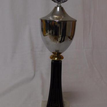 Silberner Pokal auf schwarzem Sockel mit goldener Verzierung und Prägedetails, beschriftet mit "10 Jahre VK 84 DAARMSTADT, 1. Platz 1994".