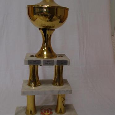 Goldener Pokal auf einer weißen Marmorsockel, mit Inschriften und einem Emblem auf der Basis.