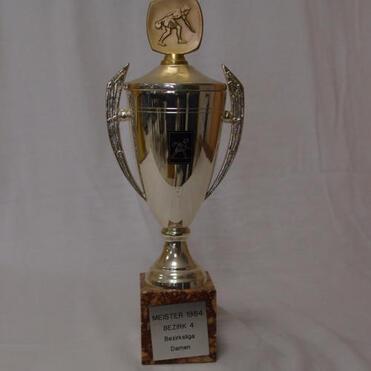 Pokal mit goldenem Deckel und gravierter Figur, beschriftet mit „Meister 1984 Bezirk 4 Damen“.