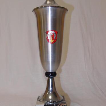 Trophäe aus Metall mit schmuckvollem Griff und Wappen auf schwarzem Marmorsockel, Hintergrund einfarbig.