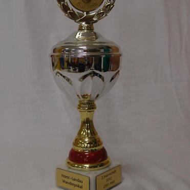 Trophäe mit goldener Medaille und Inschrift „Horst-Landau Wanderpokal“ auf einem weißen Hintergrund.