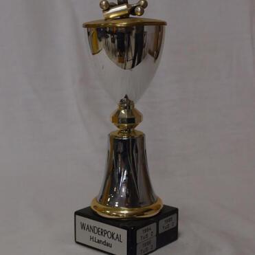 Wanderpokal mit goldenen und silbernen Elementen, beschriftet mit „H. Landau“ und Jahreszahlen auf schwarzem Sockel.