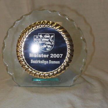 Glasplatte mit goldenem Rand, beschriftet mit „Meister 2007 Bezirksliga Damen“ und Wappen im Hintergrund.