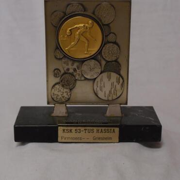 Trophäe mit goldener Medaille und Plakette, beschriftet mit „KSK 53-TUS HASSIA Firmasens – Greisheim“.