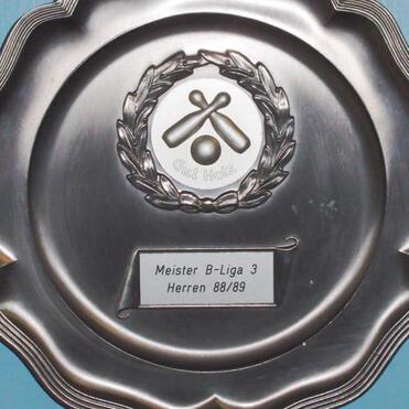 Silbernes Meisterschaftsschild mit Wappen und Beschriftung „Meister B-Liga 3 Herren 88/89“ an blauer Wand.