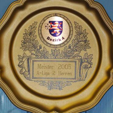 Goldene Erinnerungstafel mit dem Text „Meister 2005 A-Liga 2 Herren“ und dem Logo „Bezirk 4“.