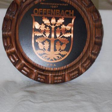Holzteller mit graviertem Wappen und Text „Hessenmeisterschaft 1987 OFFENBACH“ in Kupferfarbe.