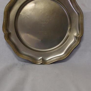 Silberner Teller mit geschwungenem Rand und Prägung in der Mitte, vor einem weißen Hintergrund.