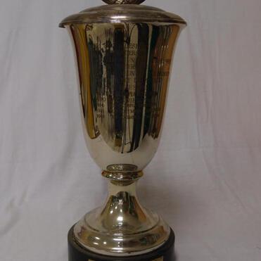 Silberner Wanderpokal mit Deckel und gravierten Schriftzügen auf schwarzem Sockel.