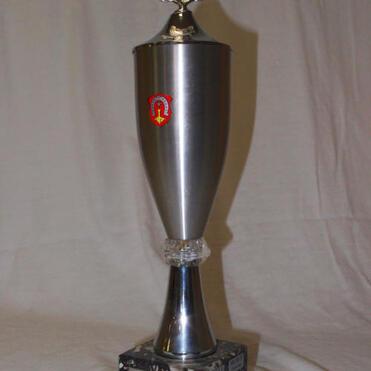 Silberner Pokal mit dekorativem Deckel, Wappen und schwarzer Basis auf hellem Hintergrund.