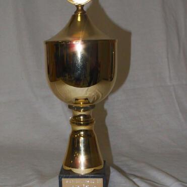 Goldener Pokal mit rundem Deckel und schwarzem Sockel, gravierte Plakette auf der Vorderseite.