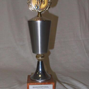 Wanderpokal aus Metall mit goldener Figur und gravierter Holzplatte, beschriftet mit „WANDERPOKAL H. Landau“.