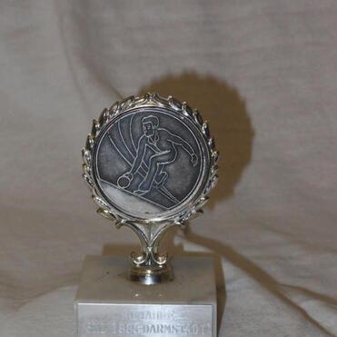 Silberner Pokal mit stilisiertem Spieler und der Aufschrift „1863 Darmstadt“ auf quadratischer Basis.