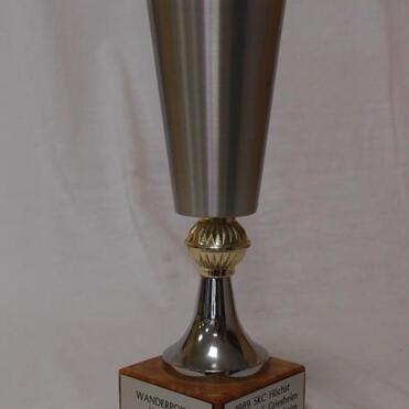 Silberner Wanderpokal mit runder Basis aus Holz, beschriftet mit Gewinnernamen von 1989 bis 1991.