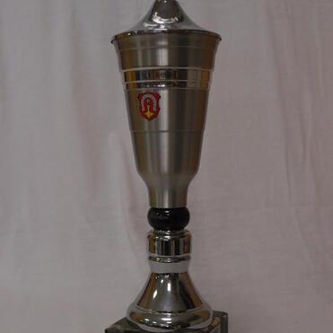 Silberner Pokal mit Wappen und Sportmotiv auf einem schwarzen Sockel. Beschriftung auf der Basis sichtbar.