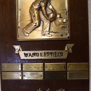 Wandertrophäe aus Holz mit bronzener Platte und Relief eines Bowlingspielers, geschmückt mit entzinnte Plaketten.