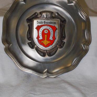 Runder, dekorativer Metallteller mit dem Wappen der Stadt Griesheim in der Mitte.